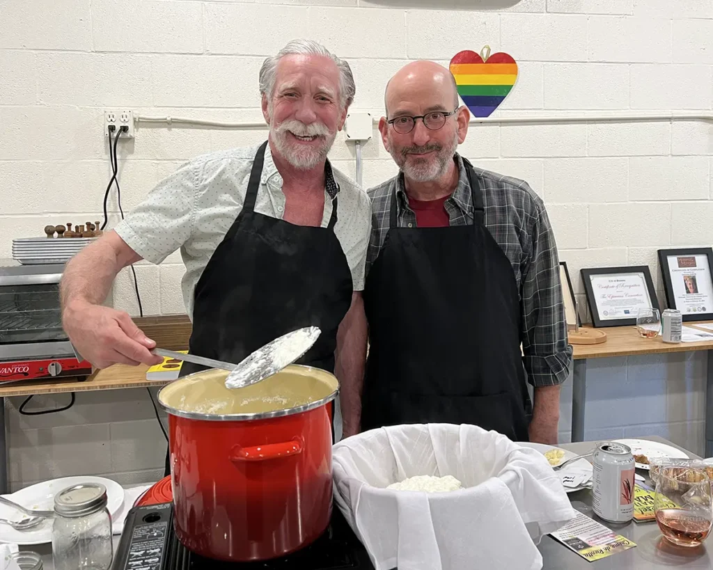 Two men smile while making fresh butter at an Epicurean Connection class