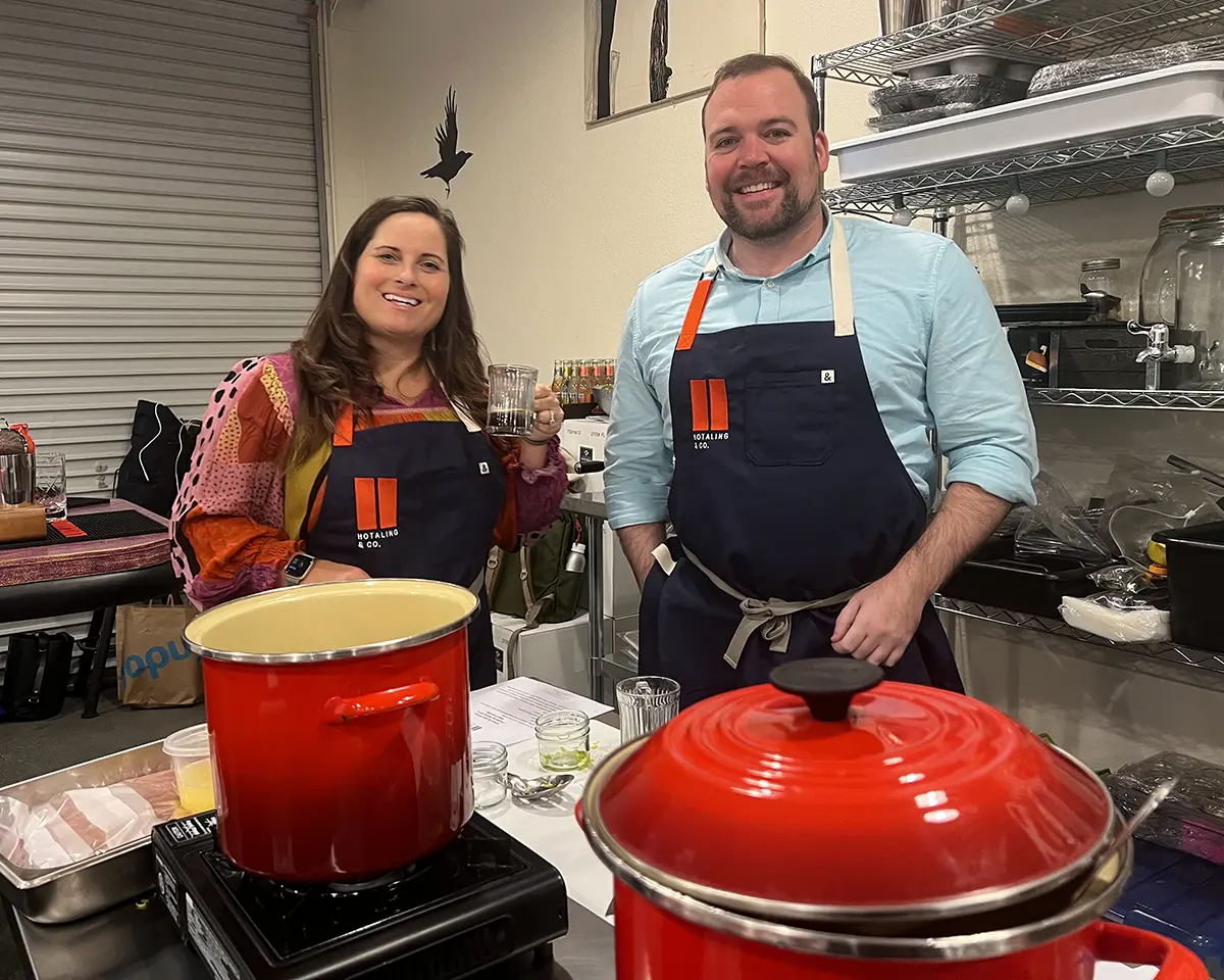 Two cheesemaking students smile wearing company branded aprons for a class