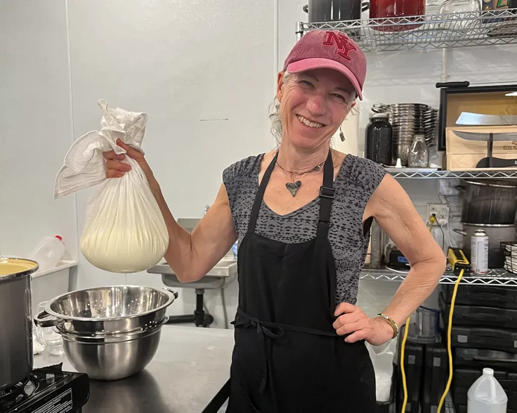 woman smiling and holding a cheesecloth full of fresh cheese